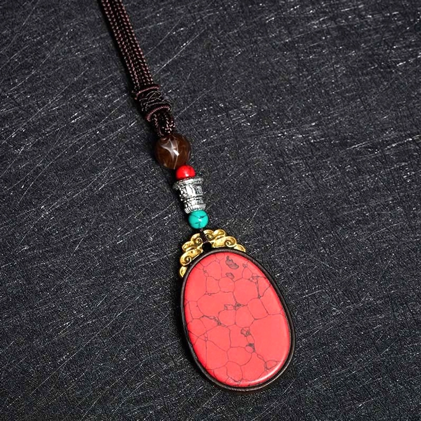 Overhead angled view of red cracked stone ebony wood pendant with decorative beaded accents and woven chain