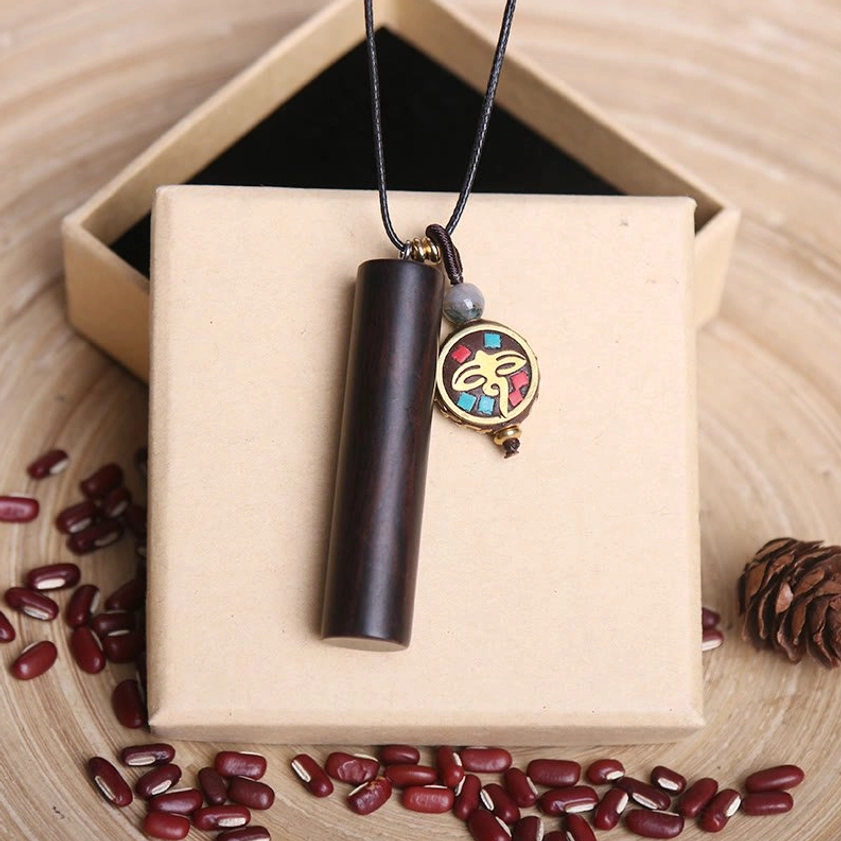 Round enamel dzi charm necklace with ebony wood tube and gold frame on wooden table with gift presentation
