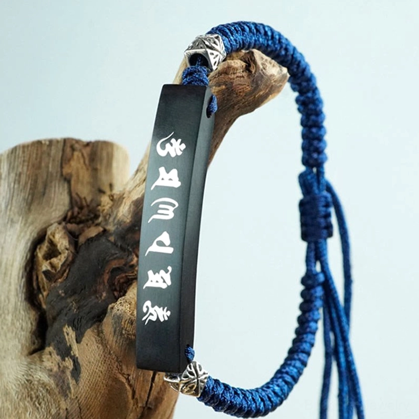 Buddhist protection bracelet with curved blue braided cord and vertical white Six True Words mantra on ebony plate with silver decorative buckles, displayed on weathered wooden stump