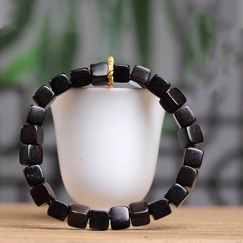 Black ebony wood square beads bracelet displayed front view on wooden table with green foliage background