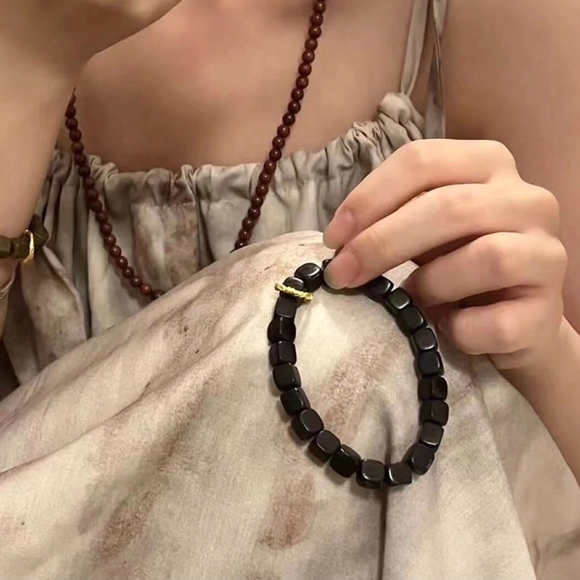 Handmade ebony wood square bead bracelet held in hand with twisted gold clasp in cozy home setting