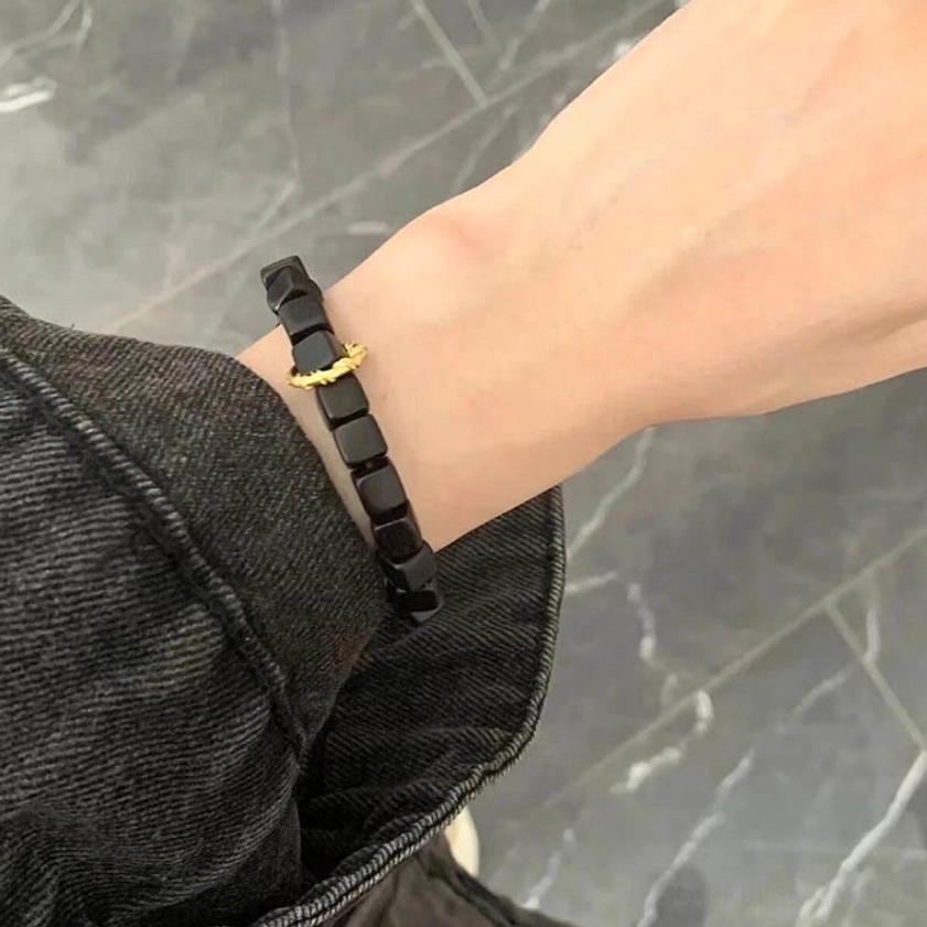 Side close-up view of ebony wood square bead bracelet on wrist with marble tabletop and twisted gold clasp