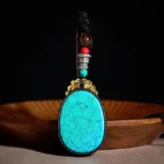Handcrafted ebony wood oval pendant necklace with turquoise cracked stone and beaded copper accents, front view on wooden display