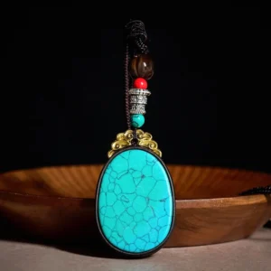 Handcrafted ebony wood oval pendant necklace with turquoise cracked stone and beaded copper accents, front view on wooden display