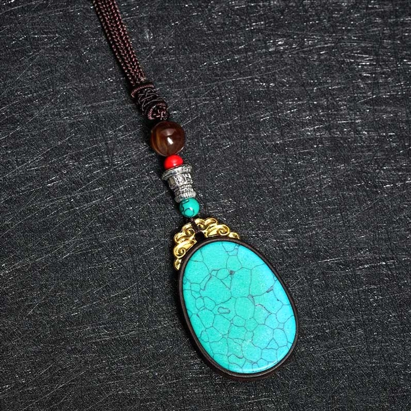 Top-down angled view of turquoise cracked stone ebony wood pendant necklace on dark fabric with brown woven cord