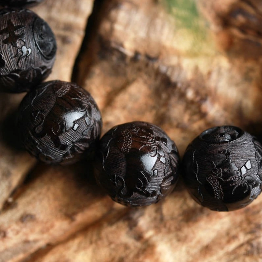 Extreme macro close-up of individual hand-engraved ebony wood yin yang bead showing intricate motifs and natural dark wood texture detail