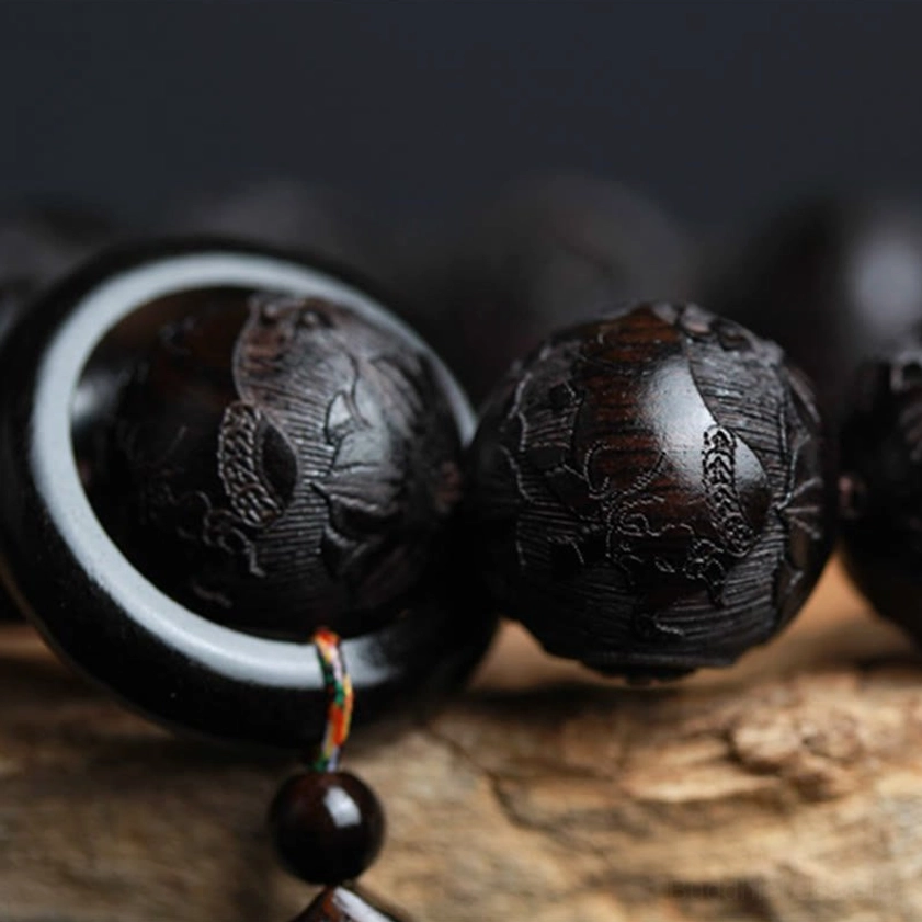 Partial view of hand-carved ebony bracelet showing individual bead details with black ring accent and colored spiritual tassel on wooden surface