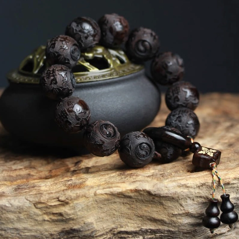 Close-up three-quarter view of carved ebony wood yin yang bracelet with black incense censer, highlighting matte wood finish and tasseled spiritual pendant