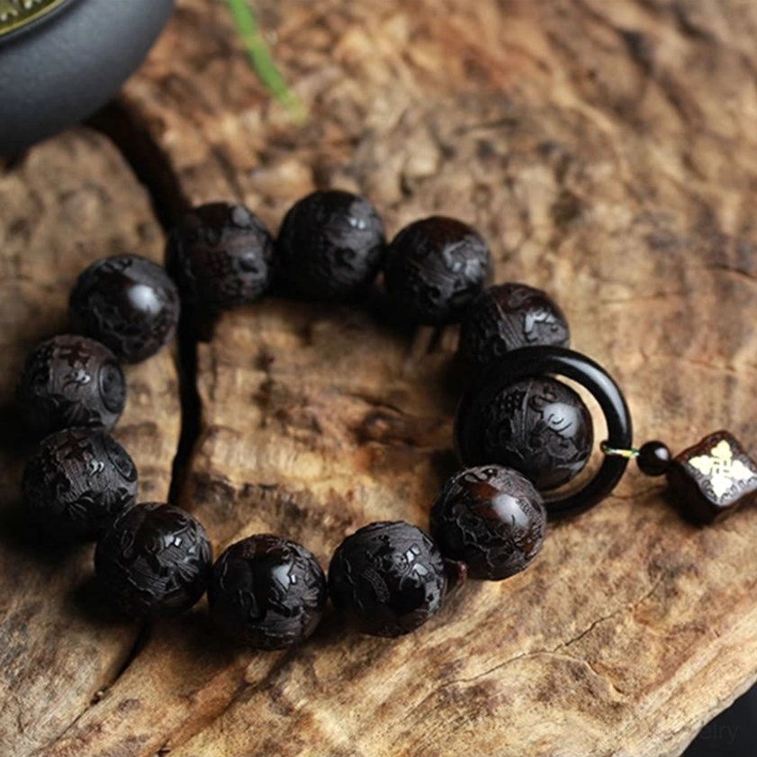 Full top-down flat lay of complete hand-carved ebony wood yin yang bracelet with all 12 beads, circular ring, and gilt decorative charm on wooden bark