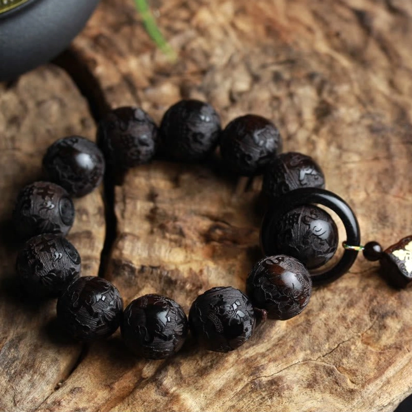 Flat lay overhead view of complete ebony wood yin yang bracelet with 12 carved beads and circular ring accent on wooden bark background