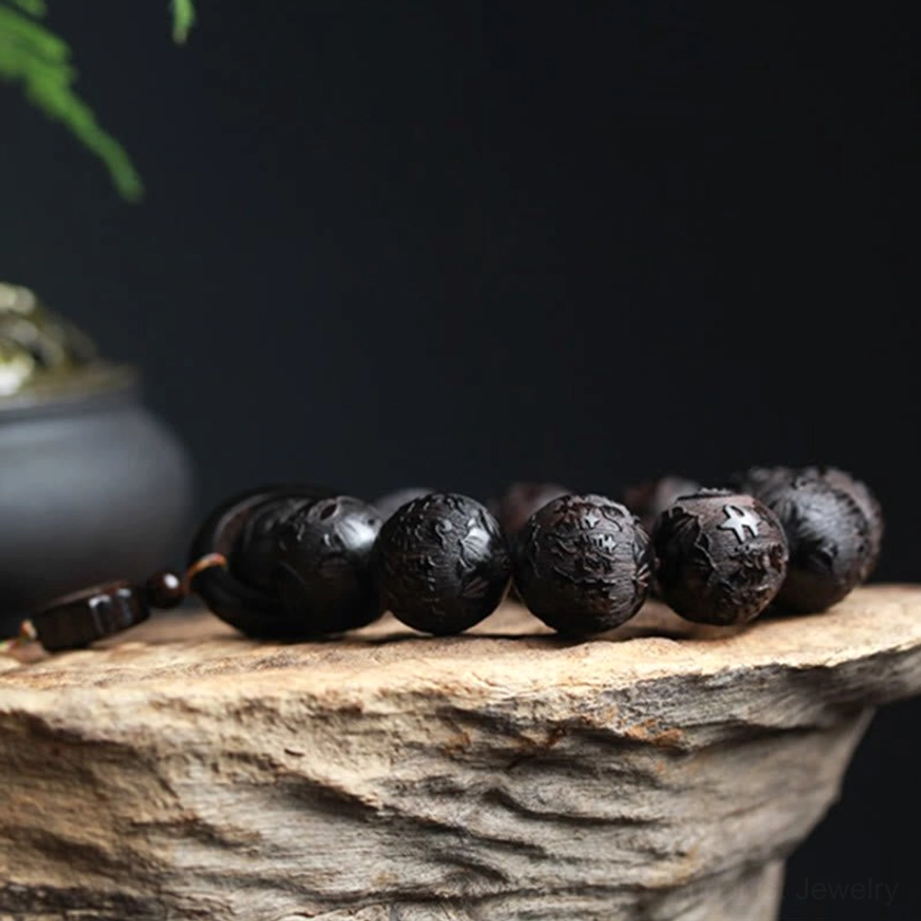Low-angle side view of complete ebony wood yin yang carved bracelet with aligned beads and small hanging pendant on minimalist dark background