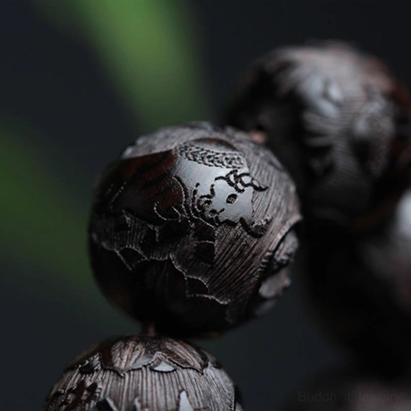 Single carved ebony wood yin yang bead in sharp focus with green foliage background, displaying detailed hand-engraved Buddhist symbol