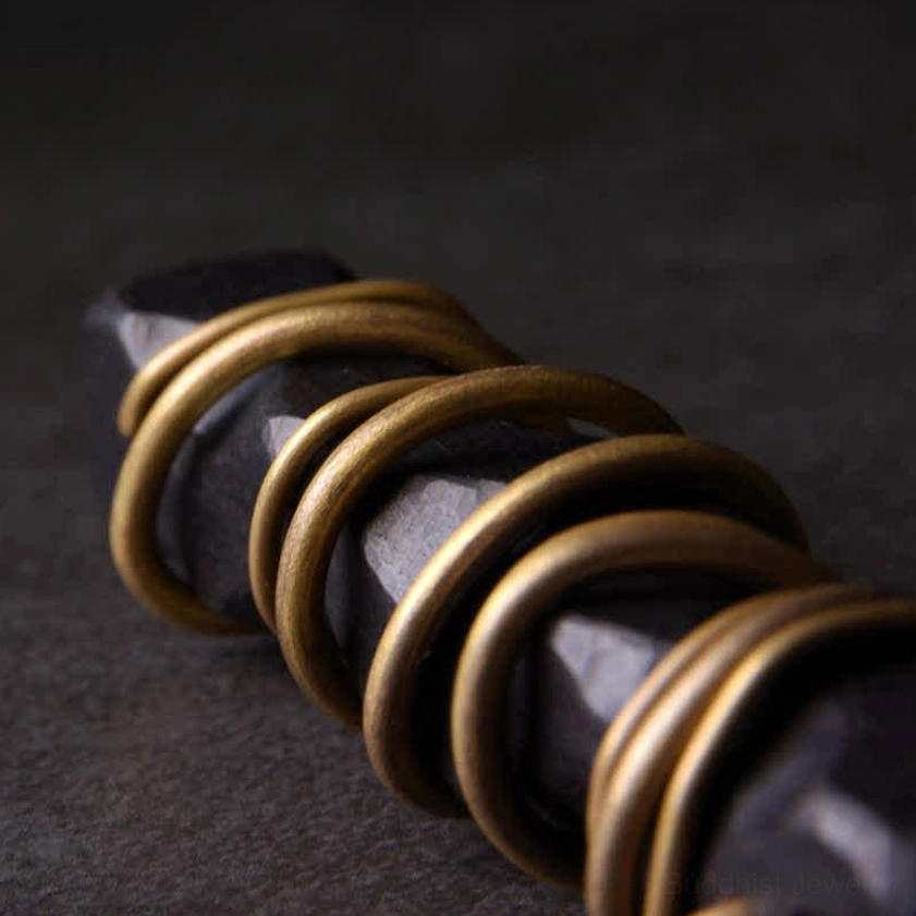 Extreme macro close-up of ebony wood zen pendant showing multi-layered brass winding and raw wood edges