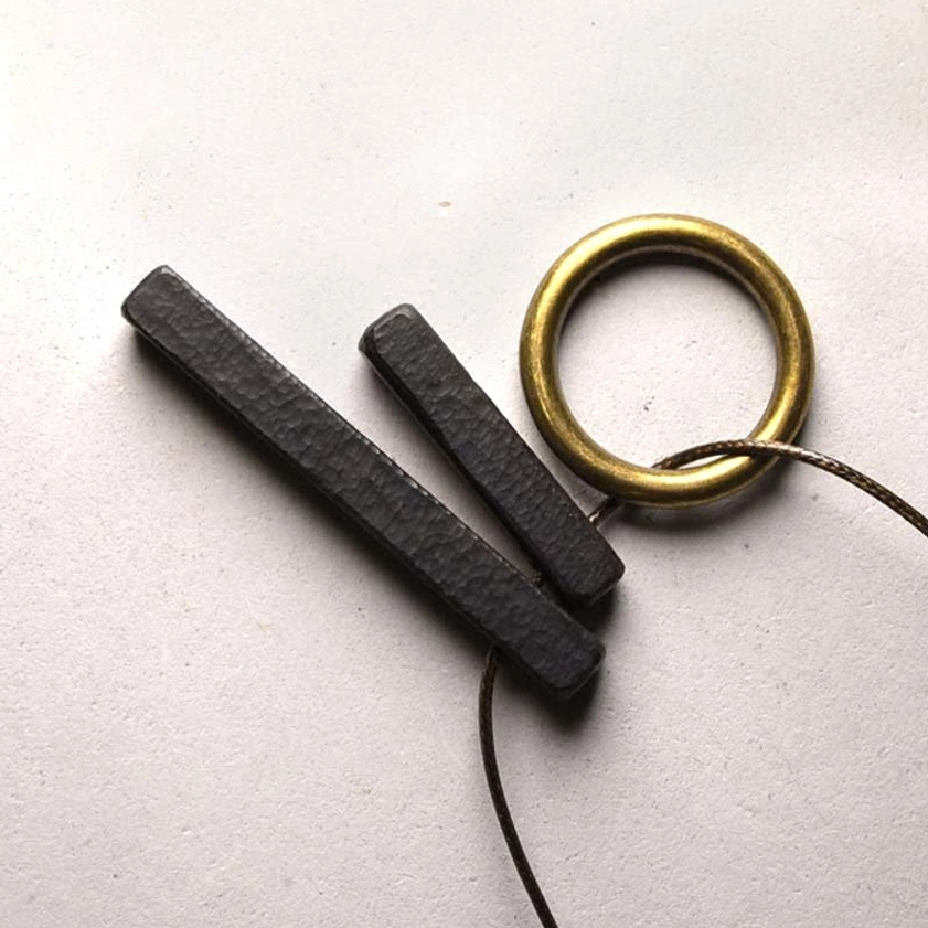 Ebony wood Zen circle Buddhist necklace pendant with brass ring and waxed cord on flat surface