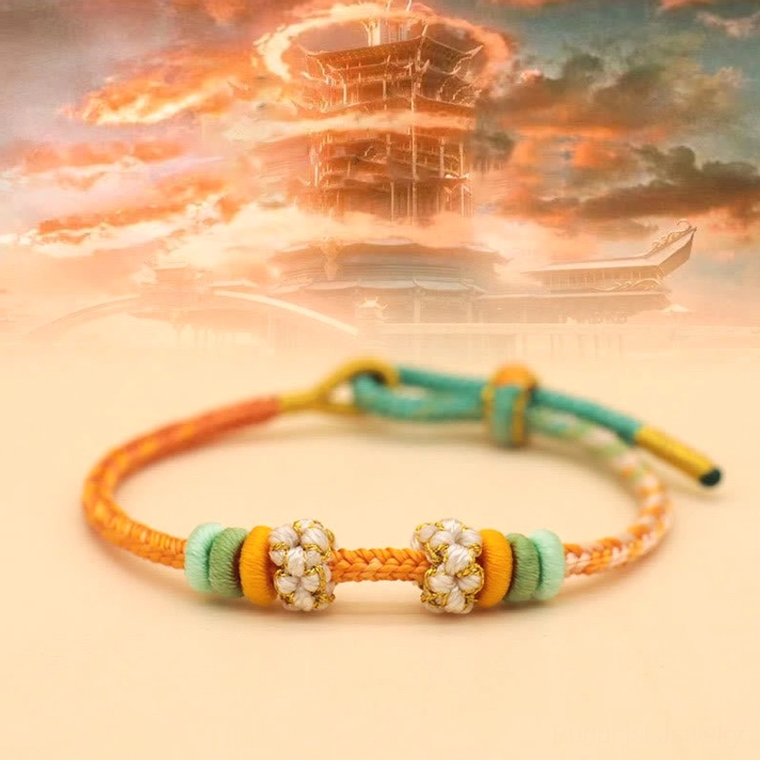 Handmade peace knot bracelet in orange, green, and yellow tones with beaded flower decoration on sunset backdrop