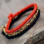 Eight-thread Buddhist peace knot braided string bracelet in layered tri-color design with red, multicolor, and black woven strands on wooden surface