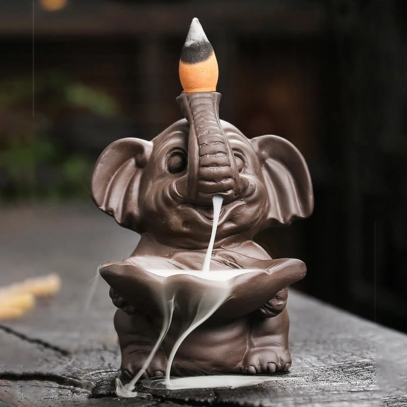 Close-up frontal view of purple clay elephant backflow incense burner with partially burnt cone and flowing smoke