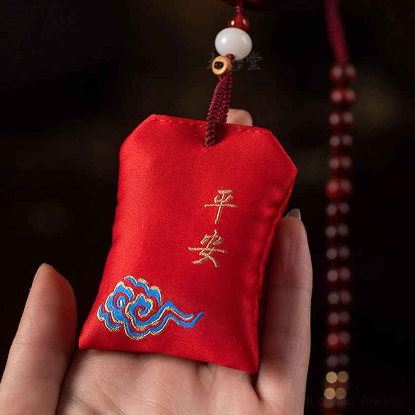 Handheld red embroidered sachet with golden peace text and blue cloud pattern showing fine embroidery detail