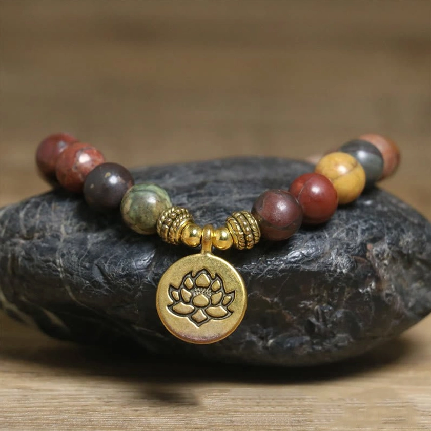 Emperor Stone anti-stress bracelet with gold lotus pendant, natural stone beads in earthy tones, resting on polished dark stone surface