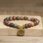 Emperor Stone lotus bracelet with gold metal lotus charm, natural variegated earthy stone beads on elastic band, displayed on wooden block