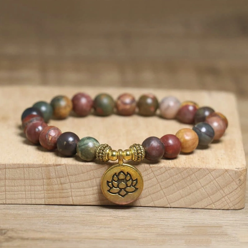 Emperor Stone lotus bracelet with gold metal lotus charm, natural variegated earthy stone beads on elastic band, displayed on wooden block