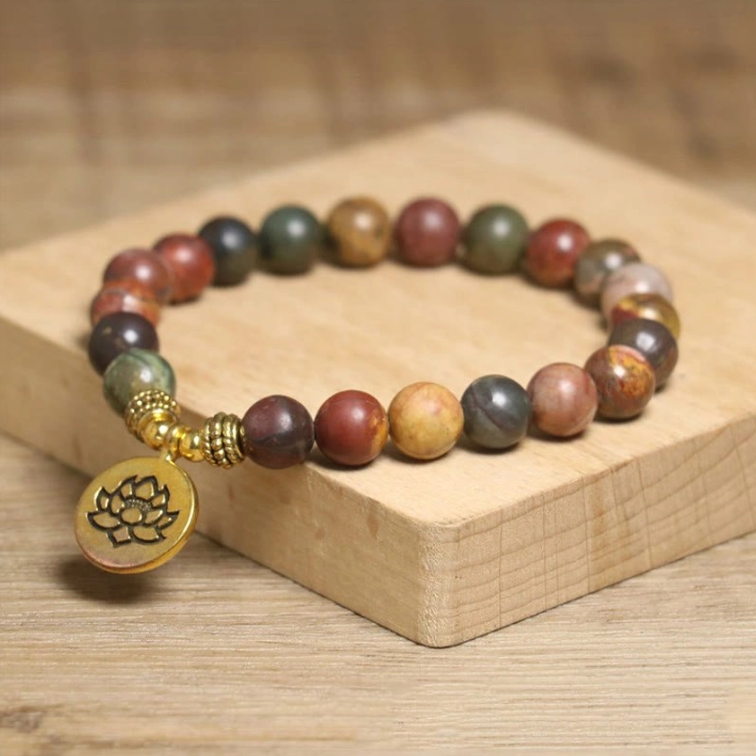 Natural Emperor Stone beaded bracelet with lotus pendant, warm multi-tone matte beads and antique gold hardware, overhead view on wooden stand