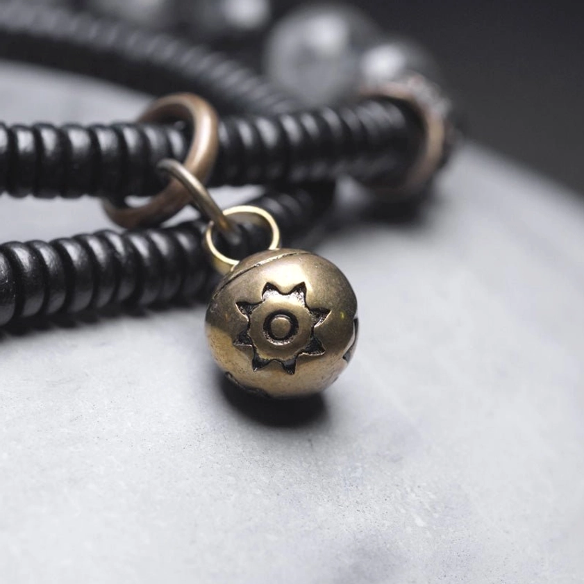 Antique bronze sun-engraved brass bell pendant with metal jump rings on elastic cord, macro photography