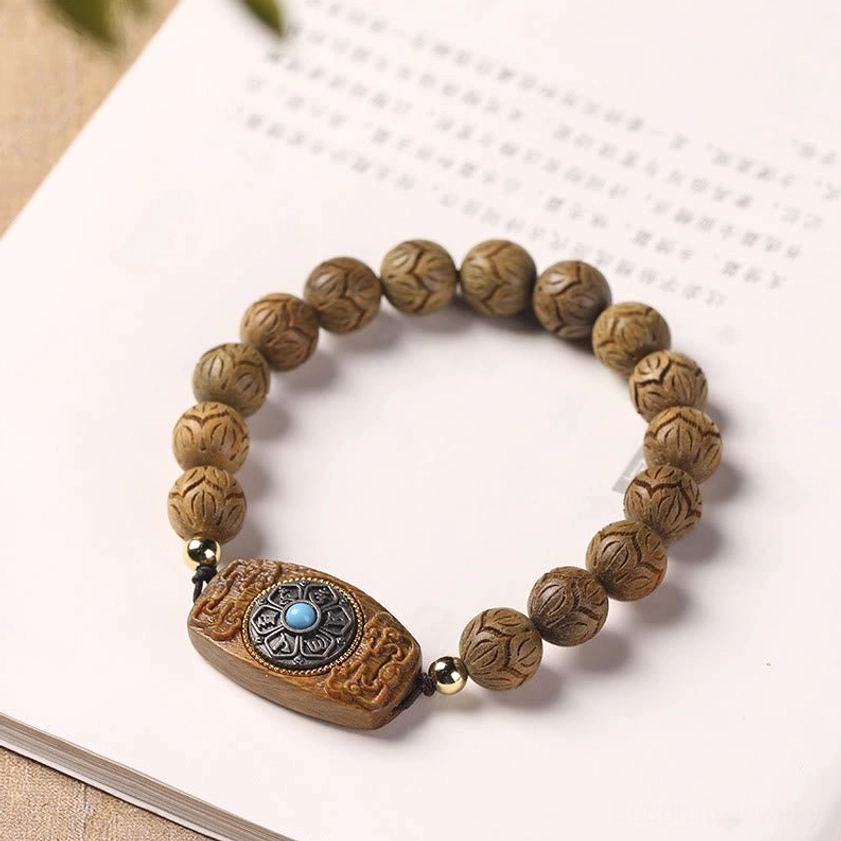 Engraved wooden bracelet resting on book page, uniform carved beads with turquoise accent