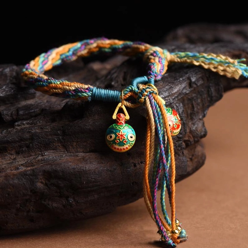 Ethnic braided rope bracelet with gold enamel swallowing beast charms and tassel accents on wooden log background