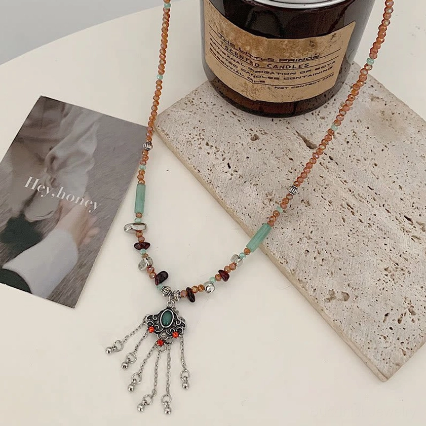 Ethnic spiritual tassel pendant necklace displayed on table with calligraphy art, showing earthy mixed beads and silver metal tassel charm for meditation practice