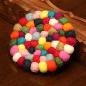 Handmade felted wool singing bowl cushion with vibrant multicolor pom-poms on wooden desktop