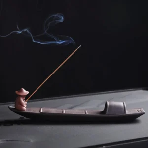 Handcrafted purple clay fisherman boat incense burner with burning incense stick, side three-quarter view showing traditional Buddhist meditation holder design