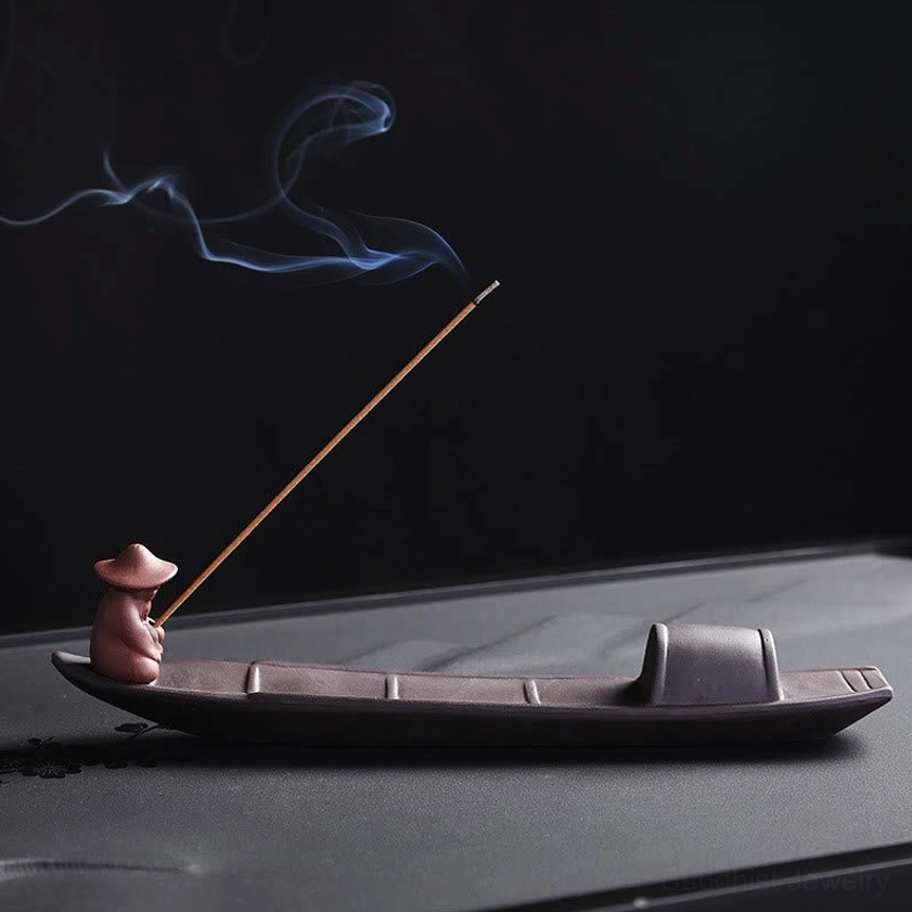 Handcrafted purple clay fisherman boat incense burner with burning incense stick, side three-quarter view showing traditional Buddhist meditation holder design