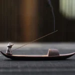 Handcrafted ceramic fisherman boat incense burner with woven cabin detail on wooden table, smoking incense stick