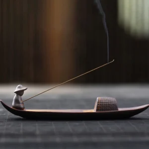 Handcrafted ceramic fisherman boat incense burner with woven cabin detail on wooden table, smoking incense stick