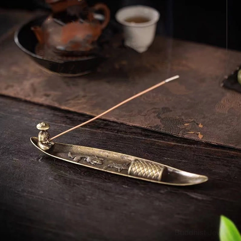 Fisherman boat incense burner with single incense stick on tea ceremony table with teapot and cup