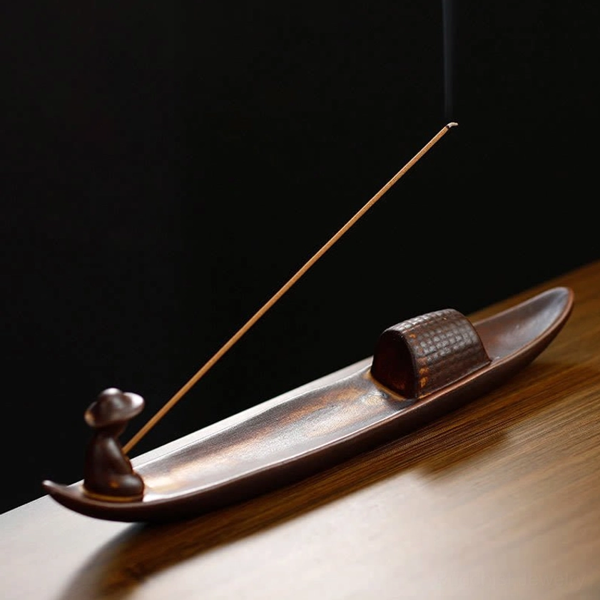 Close-up detail of ceramic incense burner showing seated fisherman figurine and boat cabin on light wood surface