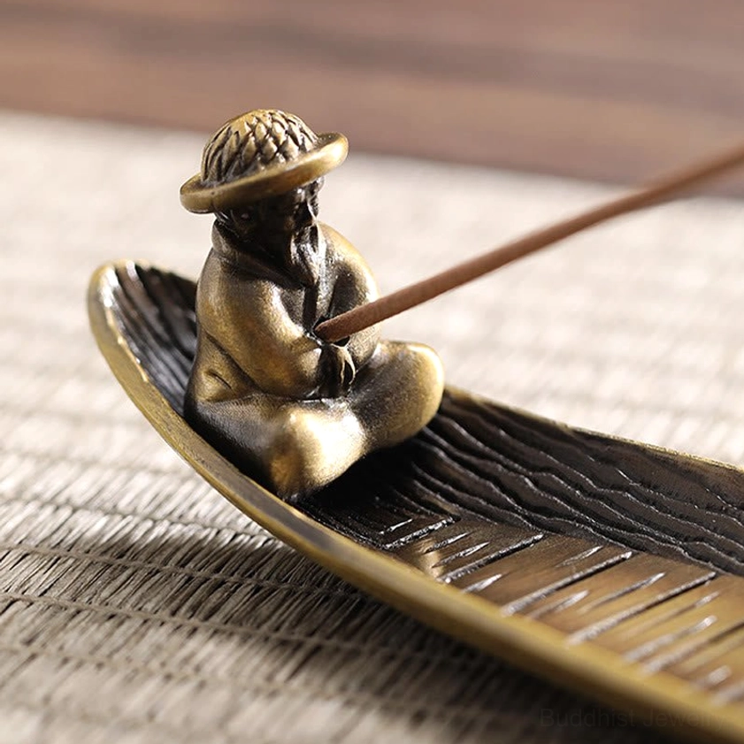 Close-up detail of bronze fisherman figurine wearing straw hat holding incense stick