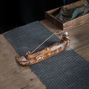 Fishing from a Lone Boat ceramic incense burner with lit incense and flowing smoke, displayed on rustic wooden table with dark woven mat
