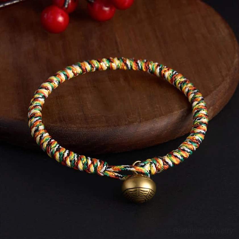 Five-color woven lucky bracelet with copper bagua charm bead photographed at eye level on wooden coaster