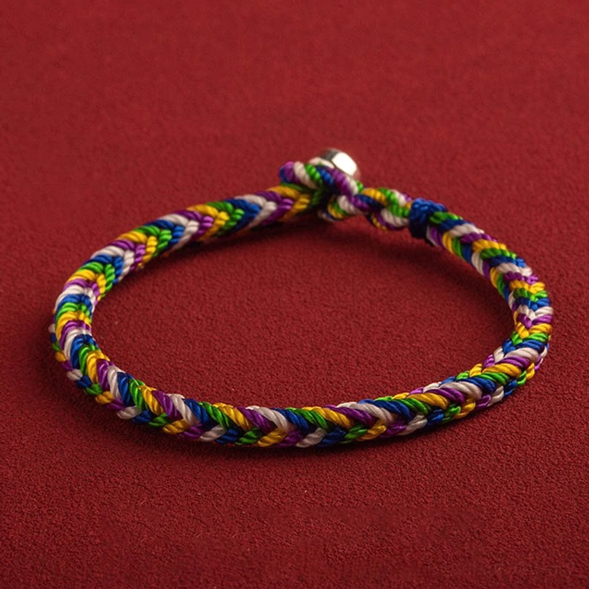 Rainbow braided Buddhist protection bracelet with silver metal clasp, overhead side view on red matte background