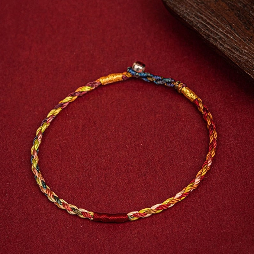Colorful Buddhist protection bracelet with five-color braid and metal clasp displayed on wooden surface
