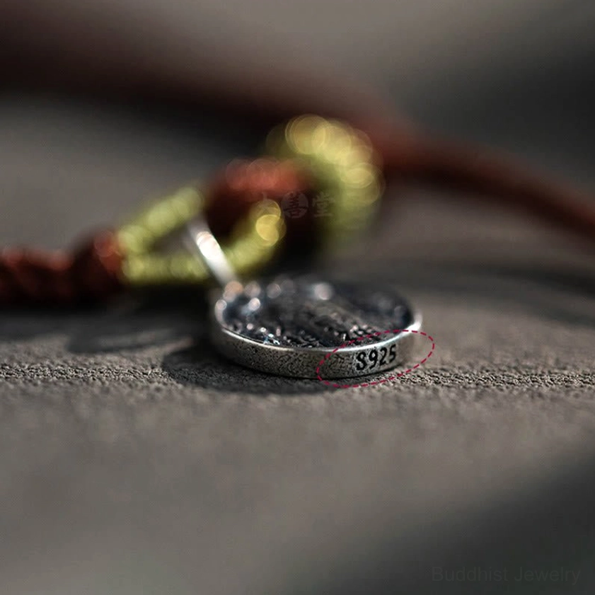 Low-angle close-up of handmade silver Five Directions Wealth Gods pendant showing engraved text and 925 marking