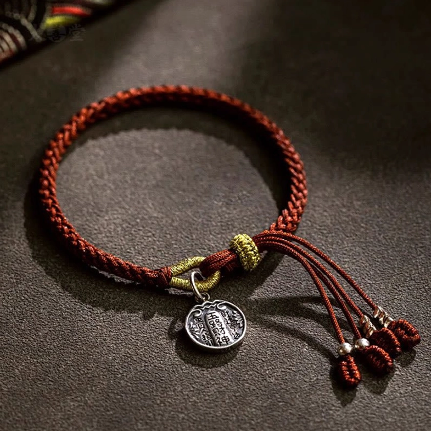 Handmade Buddhist wealth protection bracelet featuring engraved silver pendant charm and braided brown cord detail