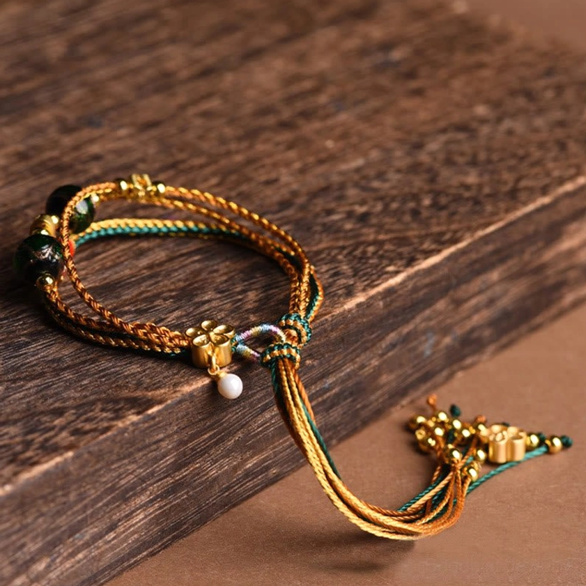 Adjustable five elements braided healing bracelet featuring white pearl pendant and brown-gold woven rope closure, flat lay view