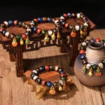 Five Elements Liuli glass bead luck bracelets arranged on wooden display with traditional Chinese ceramic vase and carved props – overhead view