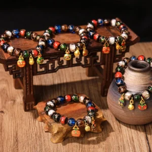 Five Elements Liuli glass bead luck bracelets arranged on wooden display with traditional Chinese ceramic vase and carved props – overhead view