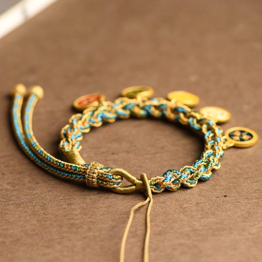 Close-up angled view of Five Gods of Wealth bracelet showing five enamel gold deity pendants and intricate woven blue-green-gold texture on turquoise ceramic surface