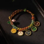 Five Gods of Wealth braided Buddhist string bracelet displayed on dark wooden surface, showing colorful rope with five enamel deity pendants and adjustable knots