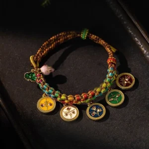 Five Gods of Wealth braided Buddhist string bracelet displayed on dark wooden surface, showing colorful rope with five enamel deity pendants and adjustable knots